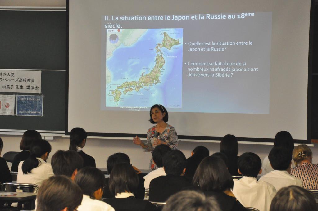 モニターに映る日本地図と、モニターの前で学生たちの向って話をしている山田大使の写真