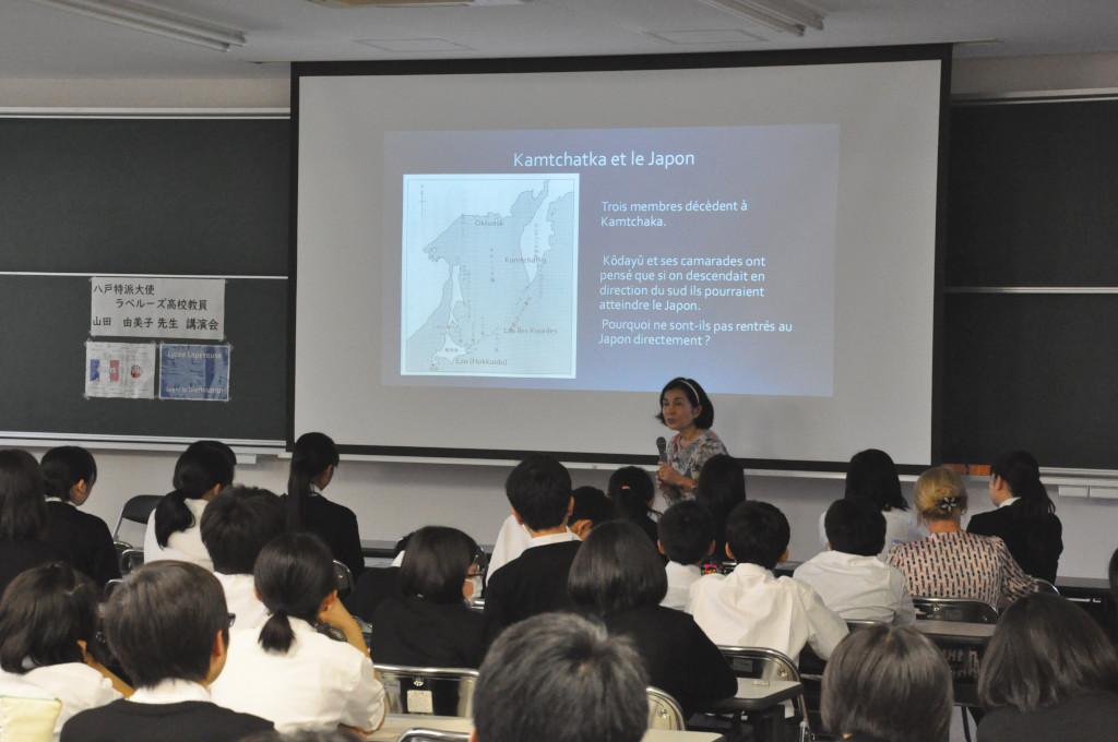 モニターの右側で学生たちに向かって話をしている山田大使の写真