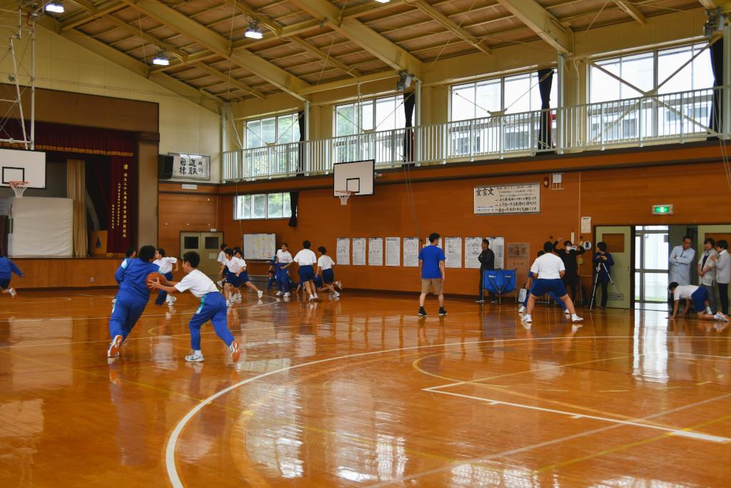 体育館にてバスケットのドリブルの練習などをしている体操服を着た生徒たちの写真