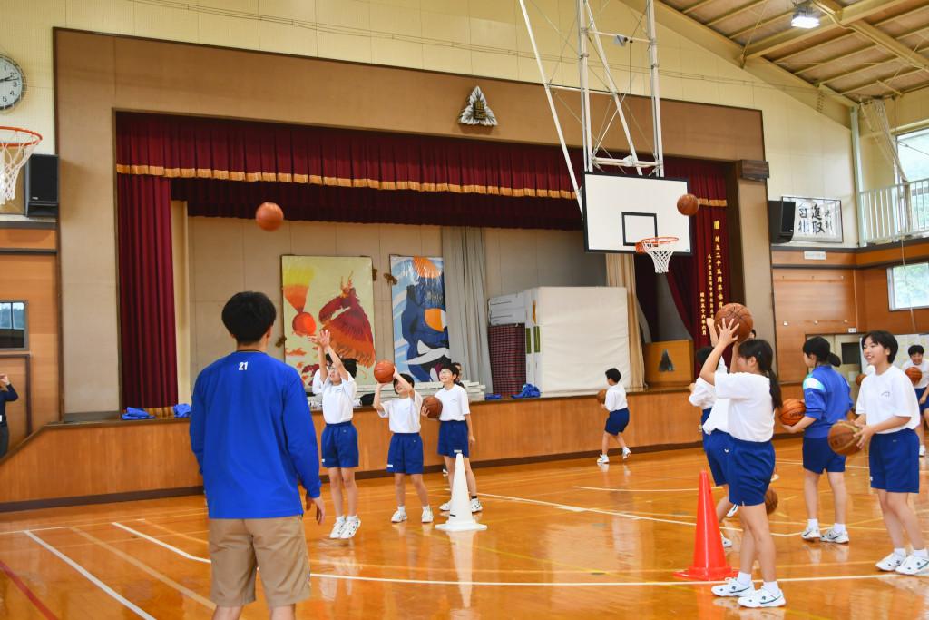 体育館にてバスケットボールのシュート練習をしている体操服を着た生徒たちの写真