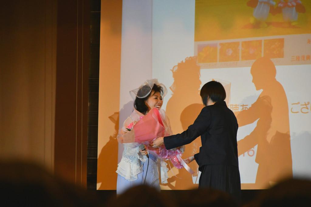 舞台の上で女子生徒から花束を受け取っている吉岡さんの写真