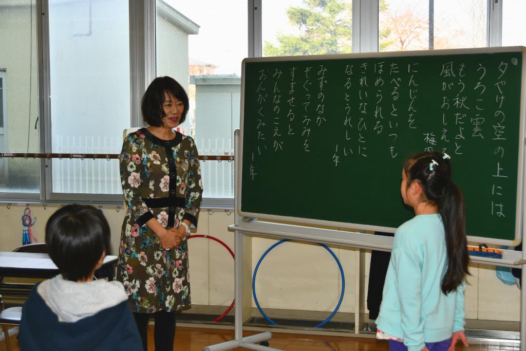 黒板の前に立って挨拶をしている女子児童と向かい合って話を聞いている梅内さんの写真