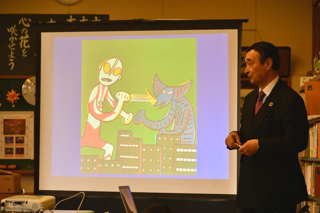 イラストの写ったモニターの横に立って説明をしている野田先生の写真