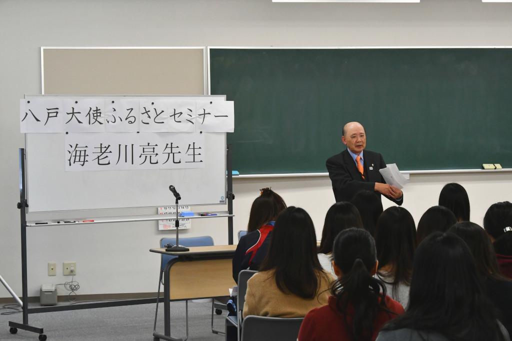 学生たちの前で、紙を持って話をしている海老川さんの写真