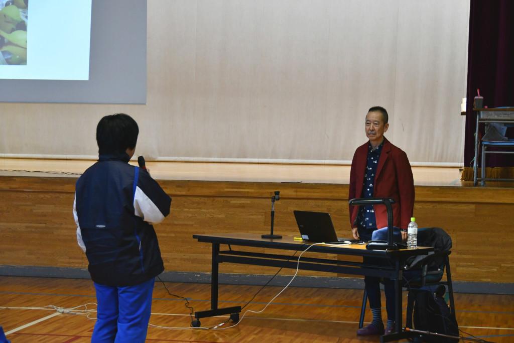 代表であいさつをしている男子生徒と、向かい合う位置に立って話を聞いている関橋さんの写真