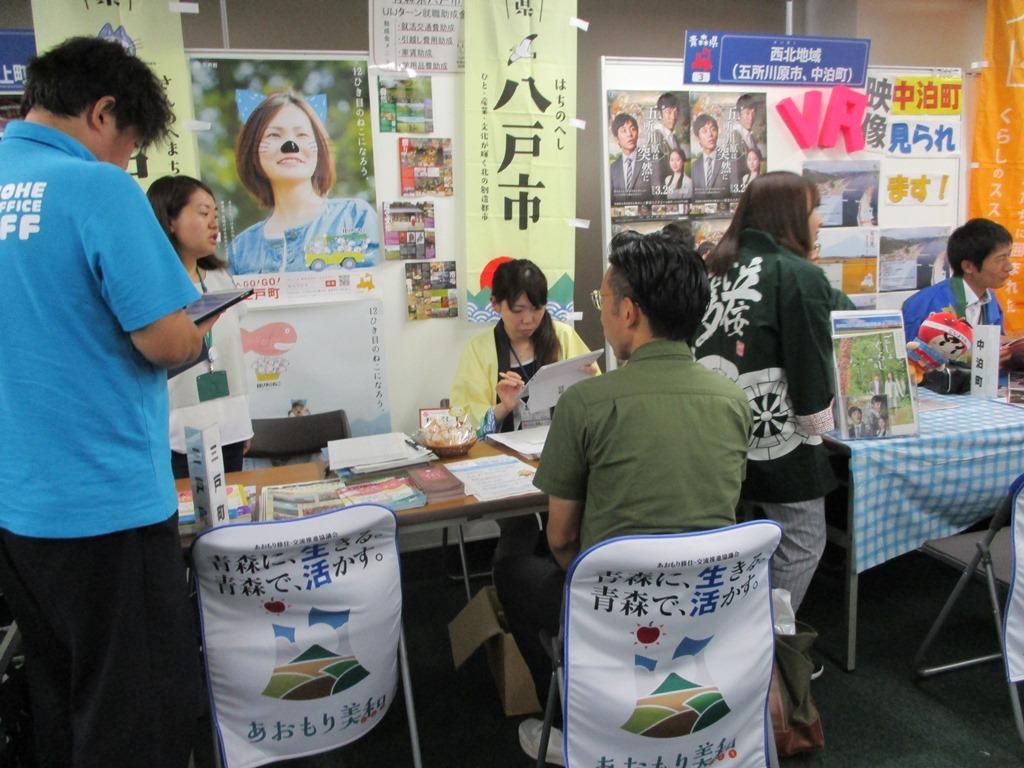 机を挟んで向かい合う、男性の参加者に女性職員が説明をしている写真