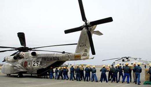 自衛隊の大型ヘリコプターの後方から荷物をリレー形式で運び出す人たちの写真