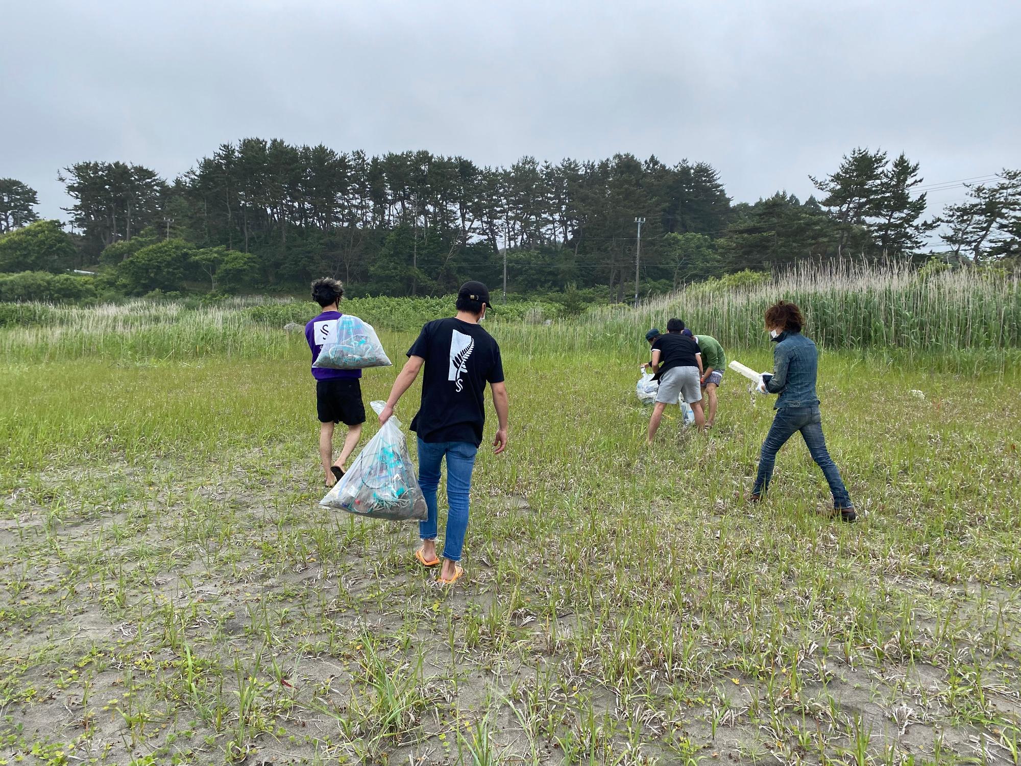 金浜海岸砂地の草が生えた場所で、重そうなボランティア用ごみ袋を運ぶ様子