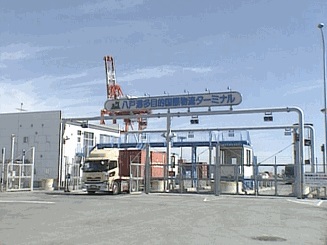 八戸港物流ターミナルの検問に、大型トラックが通過しようとしている写真