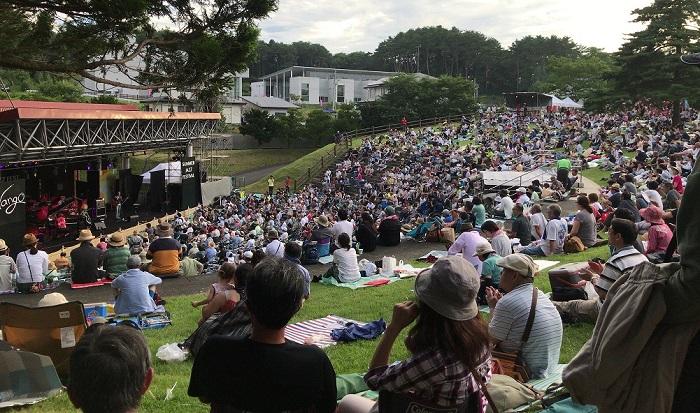 芝生に座って演奏を聴く人々の写真