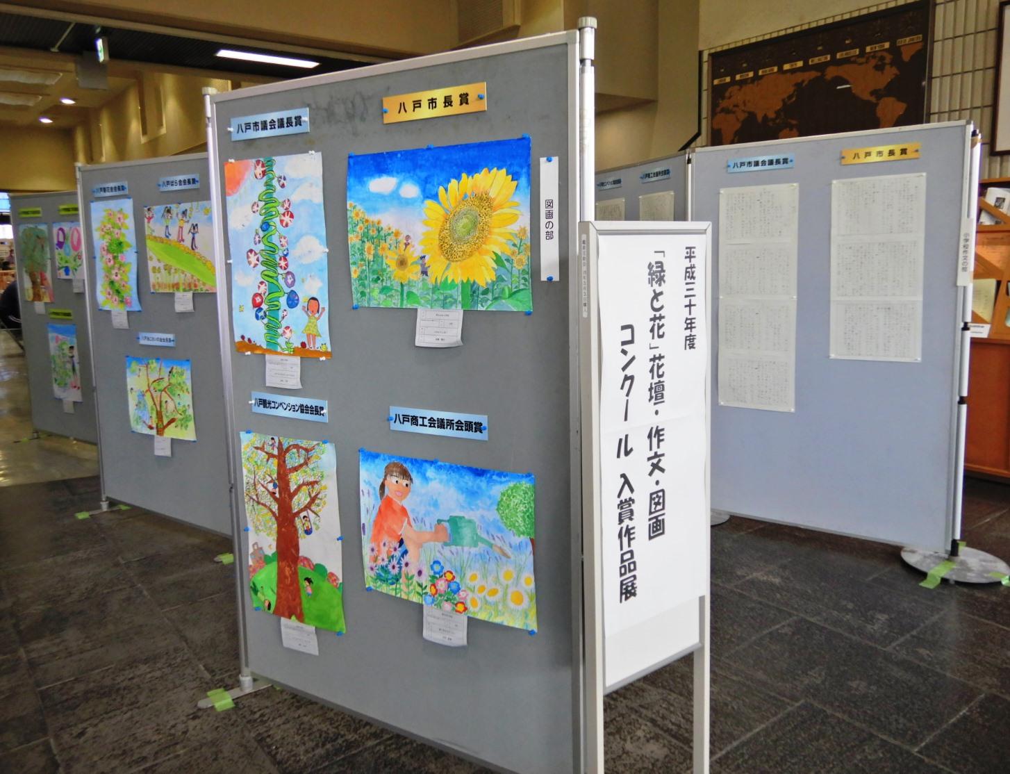平成29年度「緑と花」花壇・作文・図画コンクール入賞作品展の看板が立てられた会場のパネルにずらりと掲示されている入賞作品の写真