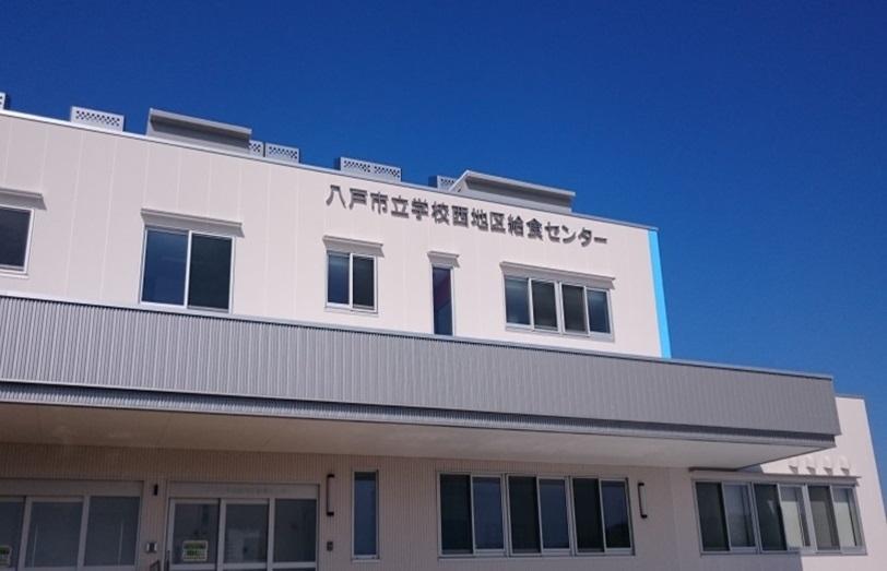 八戸市立学校西地区給食センターと壁に大きく書かれてある2階建ての給食センター建物外観の写真