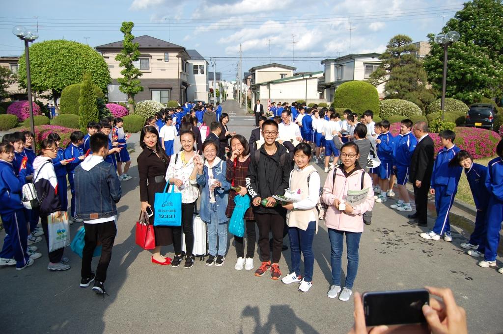 青い服を着た人たちが道の両端に立っている、中央で7名の生徒が記念撮影をしている写真