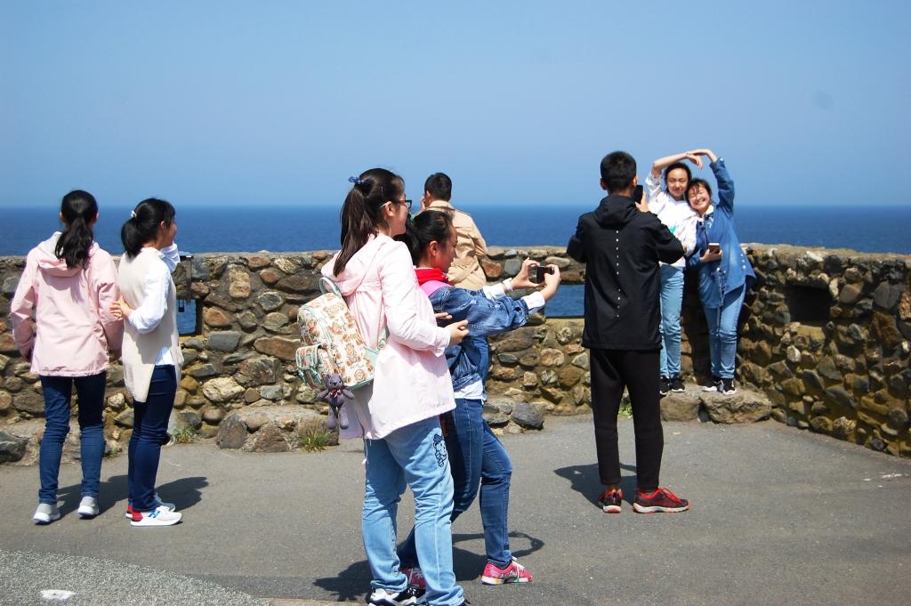 海が見える石垣の手前で記念撮影をしたり景色を眺めている人たちの写真