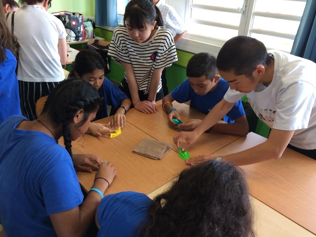 青い制服を着た現地の生徒とテーブルの上で折り紙を折っている生徒たちの写真