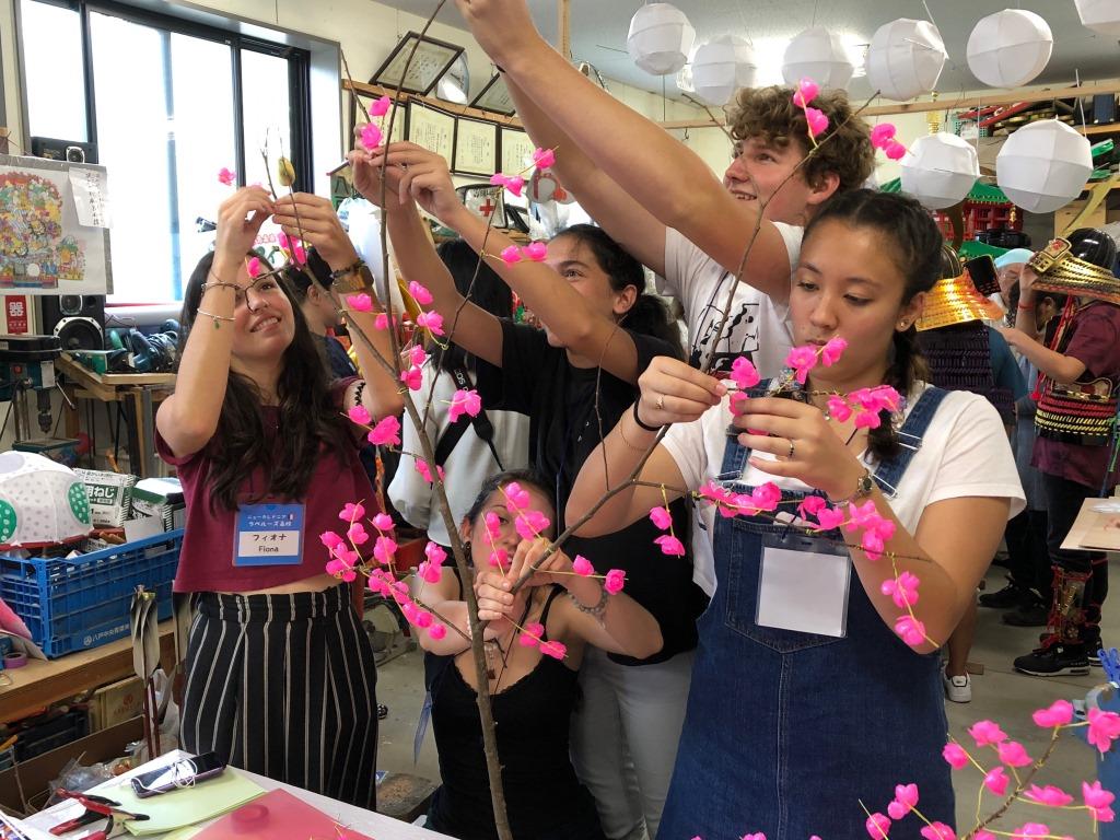 枝にピンクの造花を取り付けている外国人生徒たちの写真