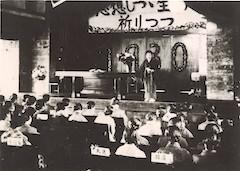 昭和5年の第一回友の会にて席に付く人々と壇上で話す人を後方から写した写真