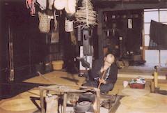 小川原湖民俗博物館内に移築した民家で、いろりに腰掛け年中行事を再現する中道等の写真