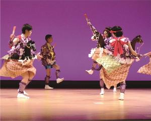 舞台にて衣装を着て片足をあげて舞を踊っている人4名が写っている写真