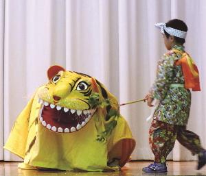 左に黄色の獅子舞のようなものがあり右側に鉢巻をまいて衣装を着ている子供が綱で引いている写真