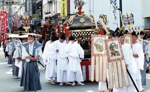 白い装束をまとった男性たちと、その後ろに神輿が続き、行列を作り町を練り歩く神幸行列の写真
