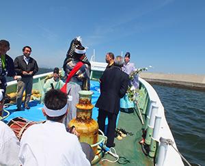 海上の船の上にて、男性らが太鼓を叩いたり舞を演じたりして、家内安全などの願いを込めた神楽を奉納している写真