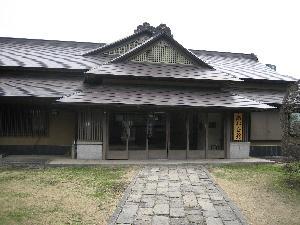 日本家屋の建物の入り口に伸びている石畳とその両脇に芝が植えられている写真