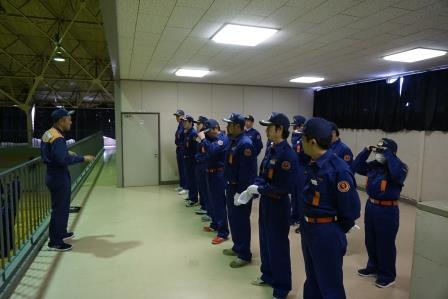 体育館の2階部分で、10名ほどの整列している消防団員が、真向いの1名の消防団員から講習を受けている様子の写真