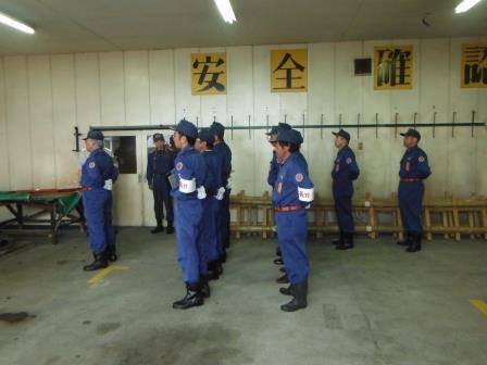10名前後のグループの消防団員が、倉庫のような場所で整列をしている様子の写真