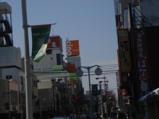 商店街の街頭に緑色の「ヴァンラーレ八戸バナーフラッグ」が取り付けられ、風になびいている様子の写真