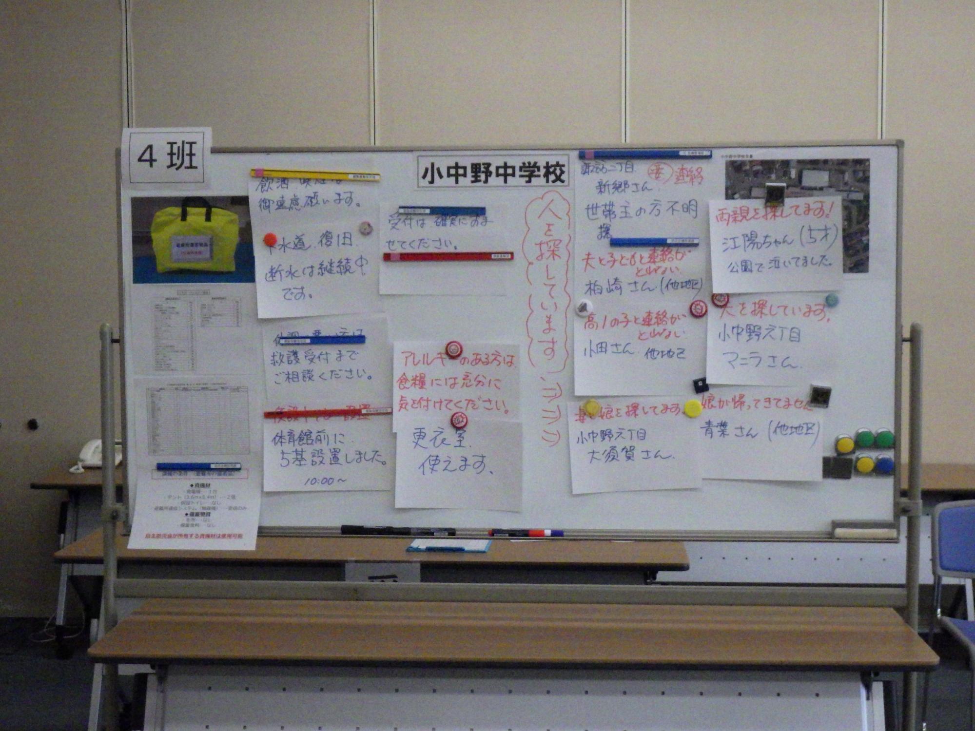 小中野中学校と書かれたホワイトボードに、避難所の連絡事項等の掲示物が張られいる写真
